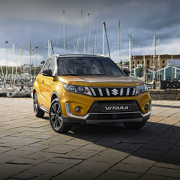 Um suzuki vitara amarelo está estacionado em uma calçada de tijolos em frente a uma marina.