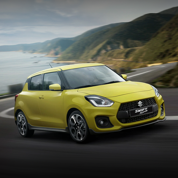 Um suzuki swift amarelo está dirigindo por uma estrada