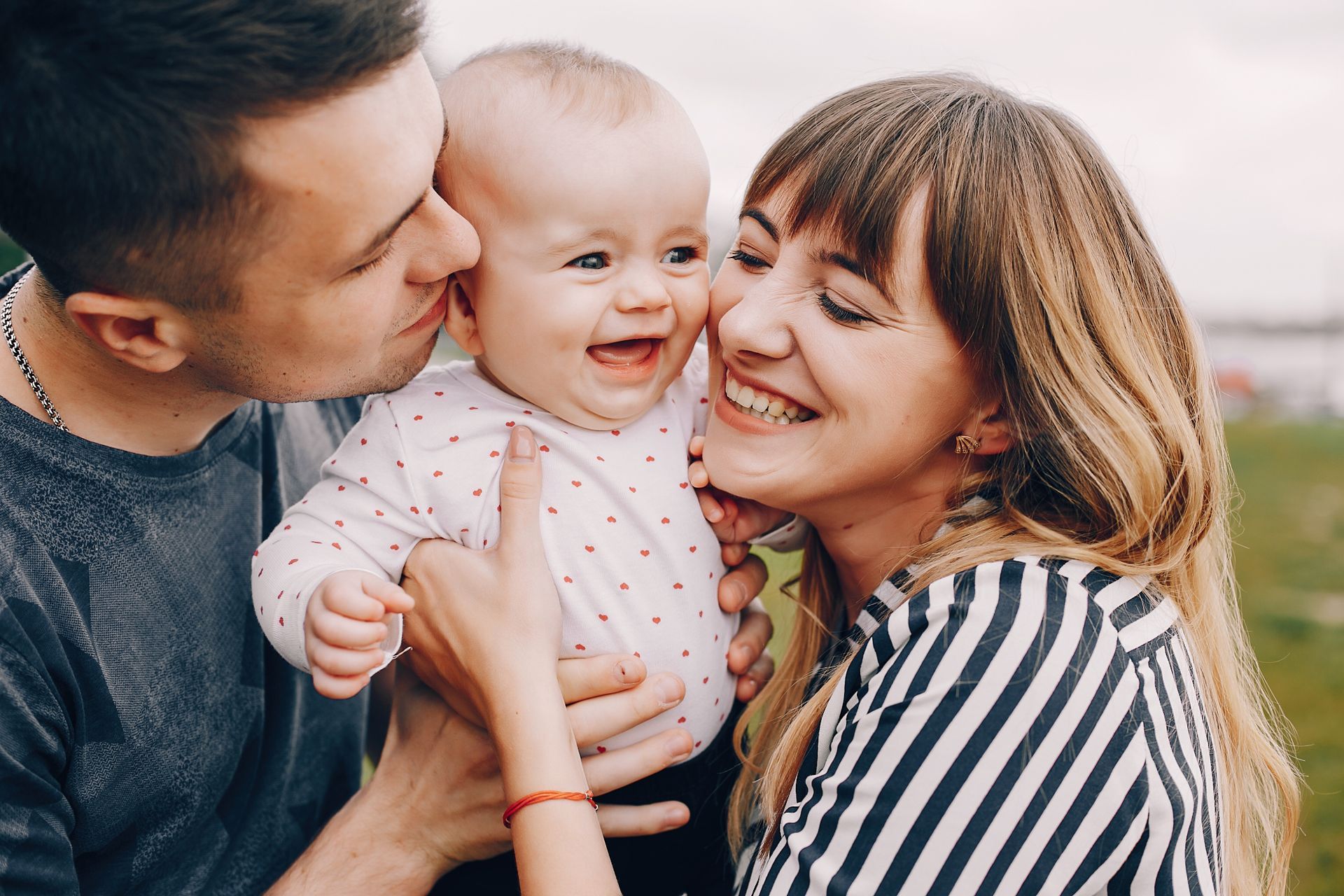 Smiling family holding a baby close, with a striped shirt and dark sweater against a warm blurred background