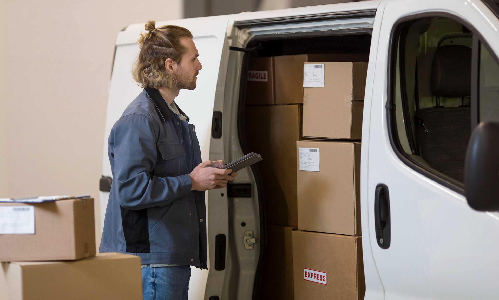 Person loading cardboard boxes into a white van from a warehouse door