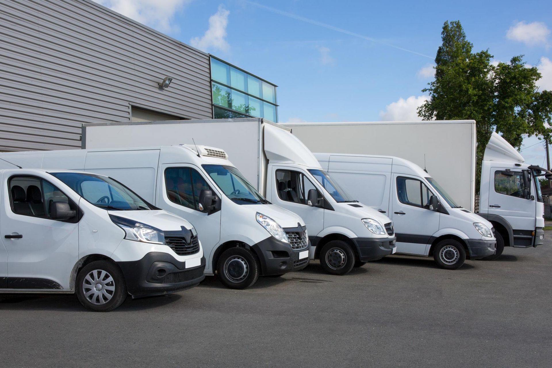 White cargo vans and box trucks parked outside a warehouse on a sunny day