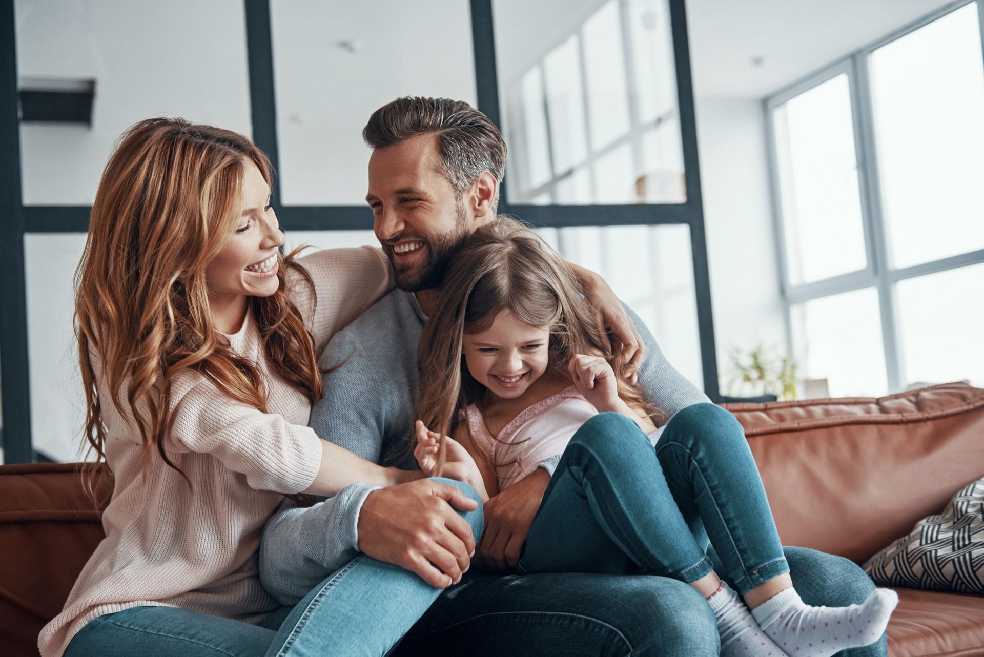 Smiling family sitting on a couch, hugging and laughing in a bright living room.