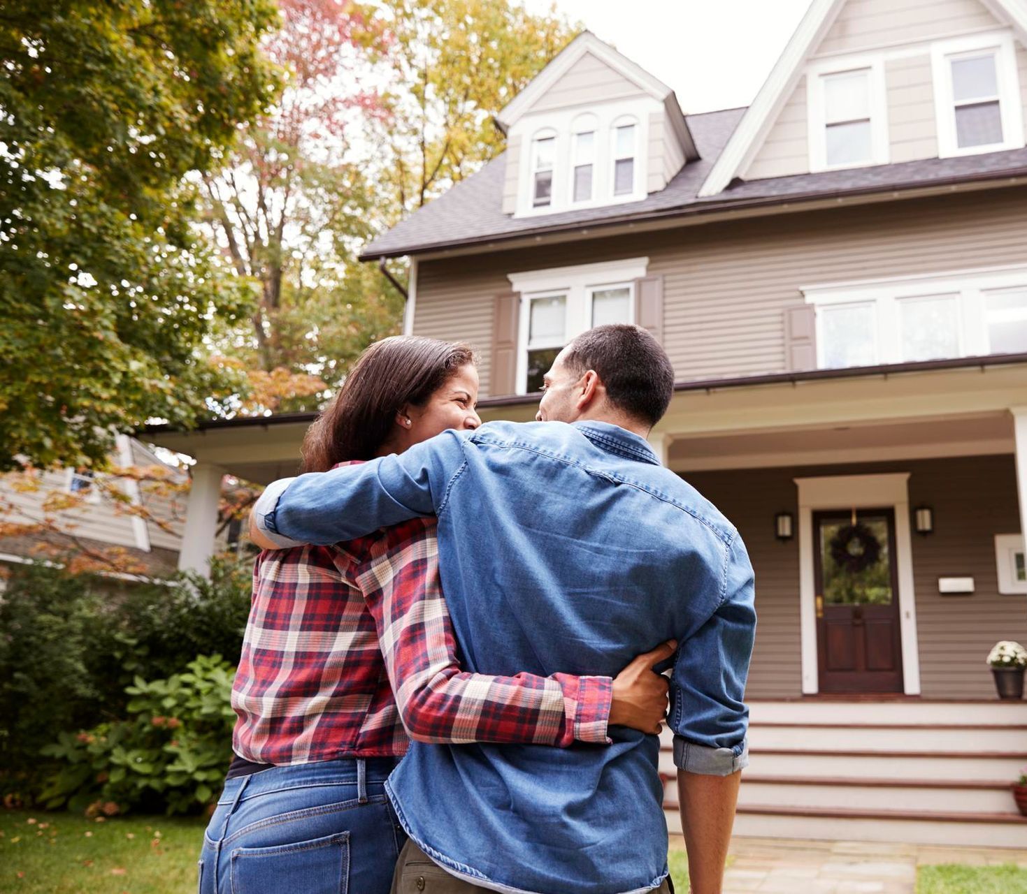 Couple hugging in front of a suburban house with a front porch and wreath on the door