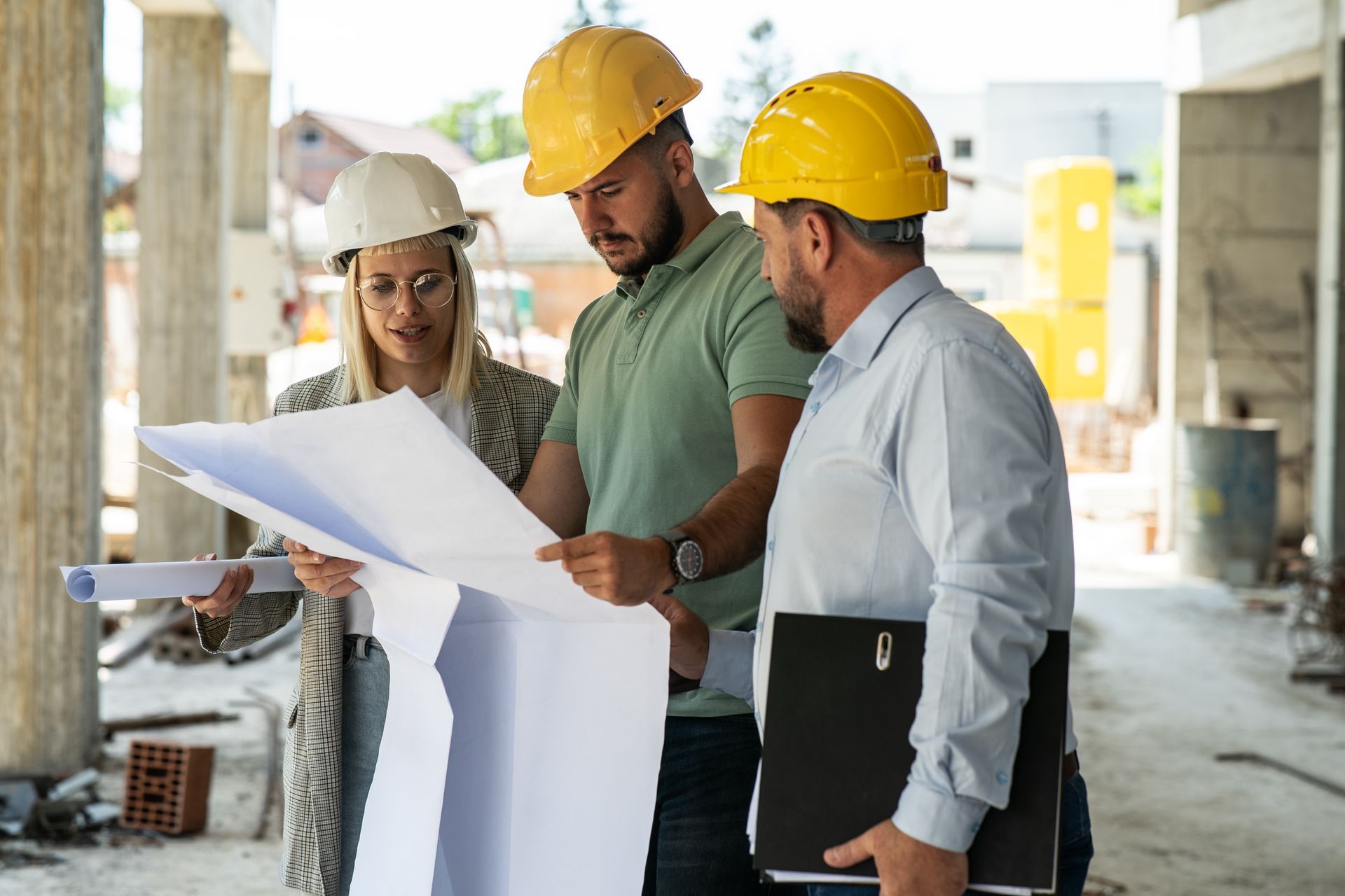 Three construction workers in hard hats reviewing blueprints at a building site