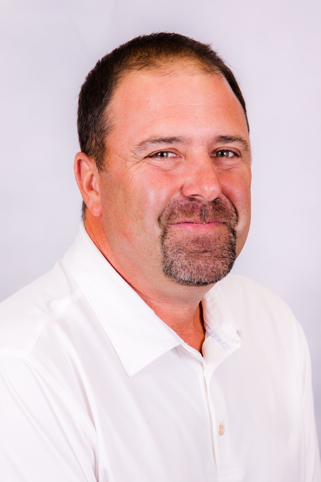 Portrait of a man in a white shirt against a light background, smiling slightly