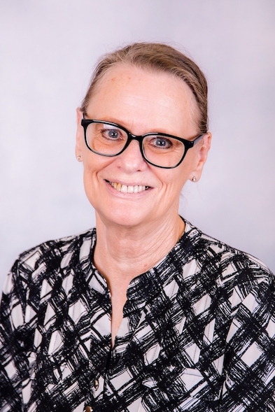 Portrait of a smiling person wearing glasses and a black-and-white patterned blouse