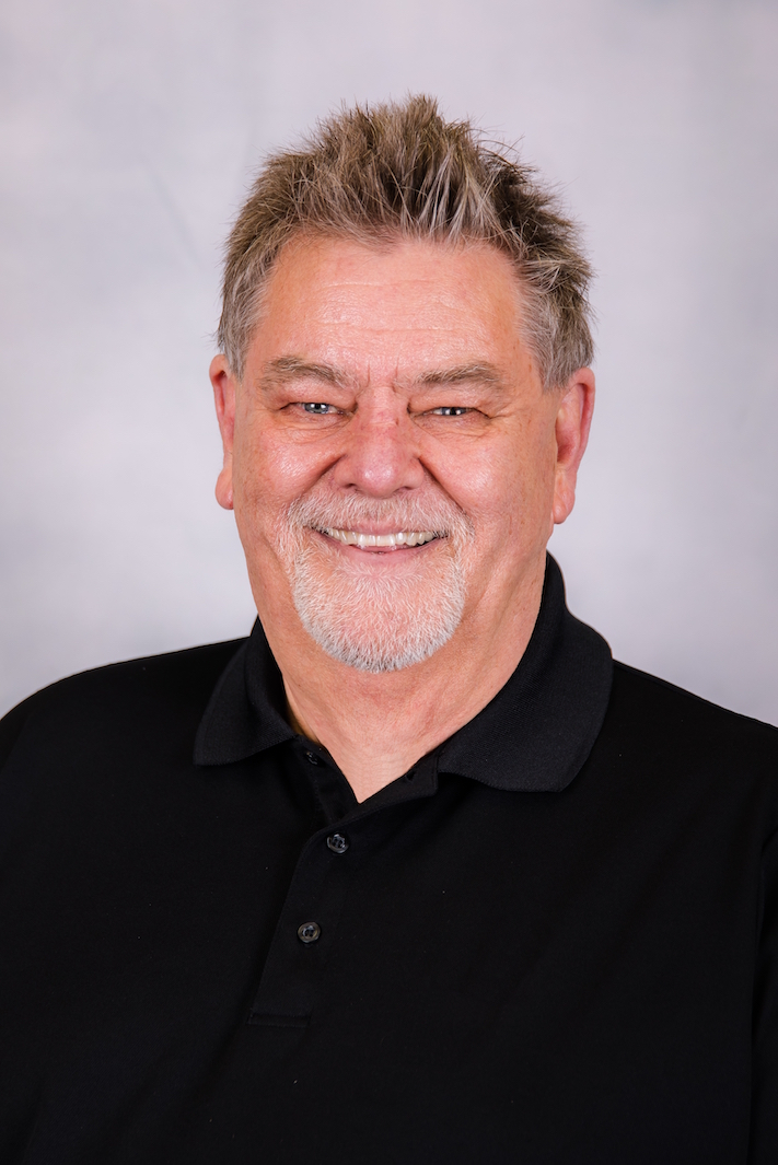 Smiling man in a black polo shirt against a light gray background