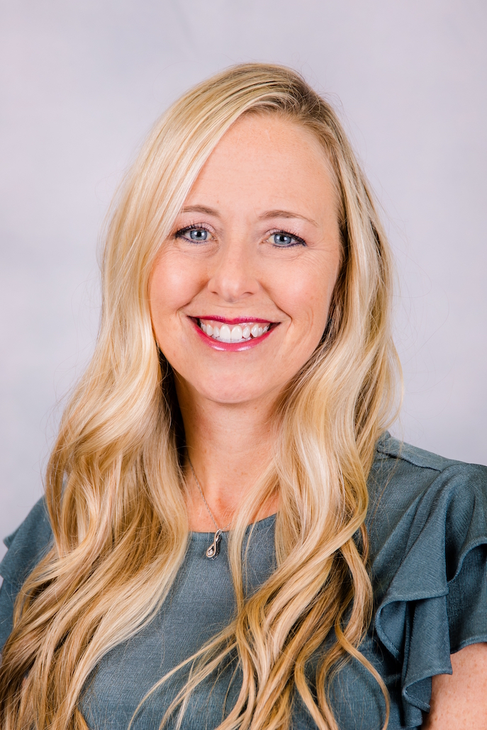 Smiling woman with long blonde hair wearing a teal ruffled top against a light background