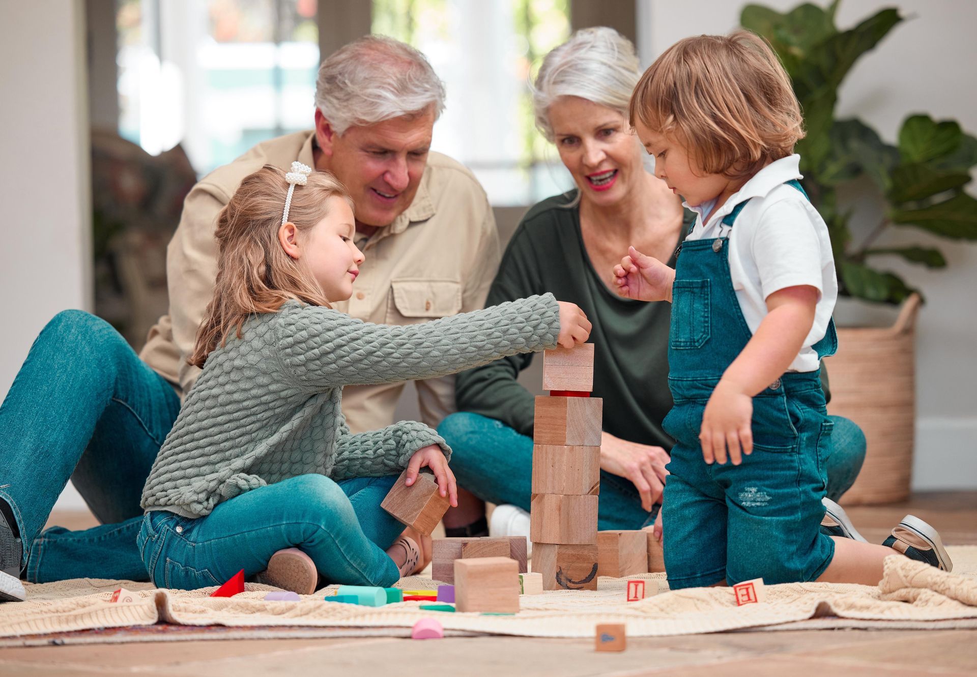 Family playing with wooden blocks on a living room floor, smiling and stacking a tower.
