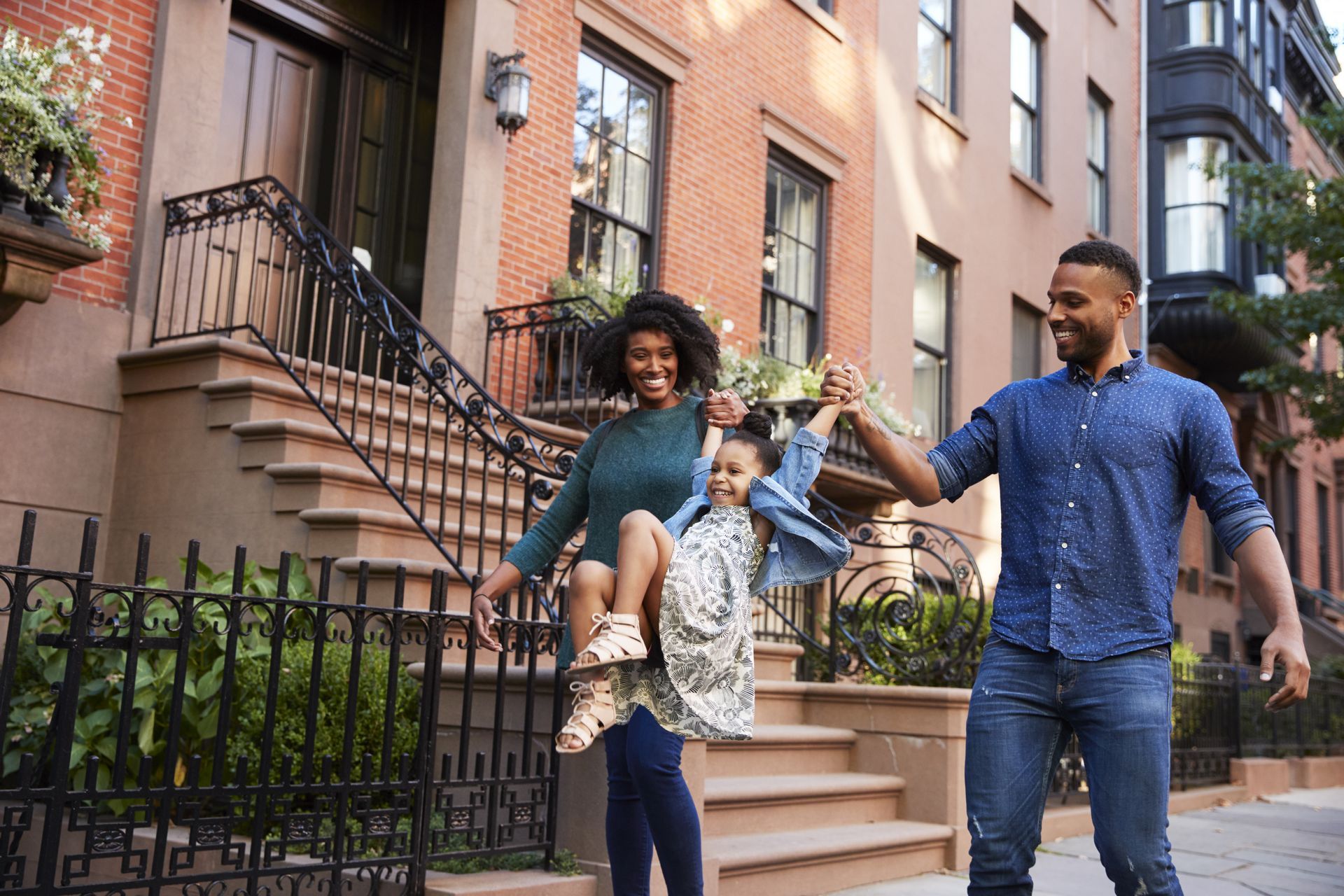 Smiling couple and child walking hand in hand past brownstone homes on a sunny street
