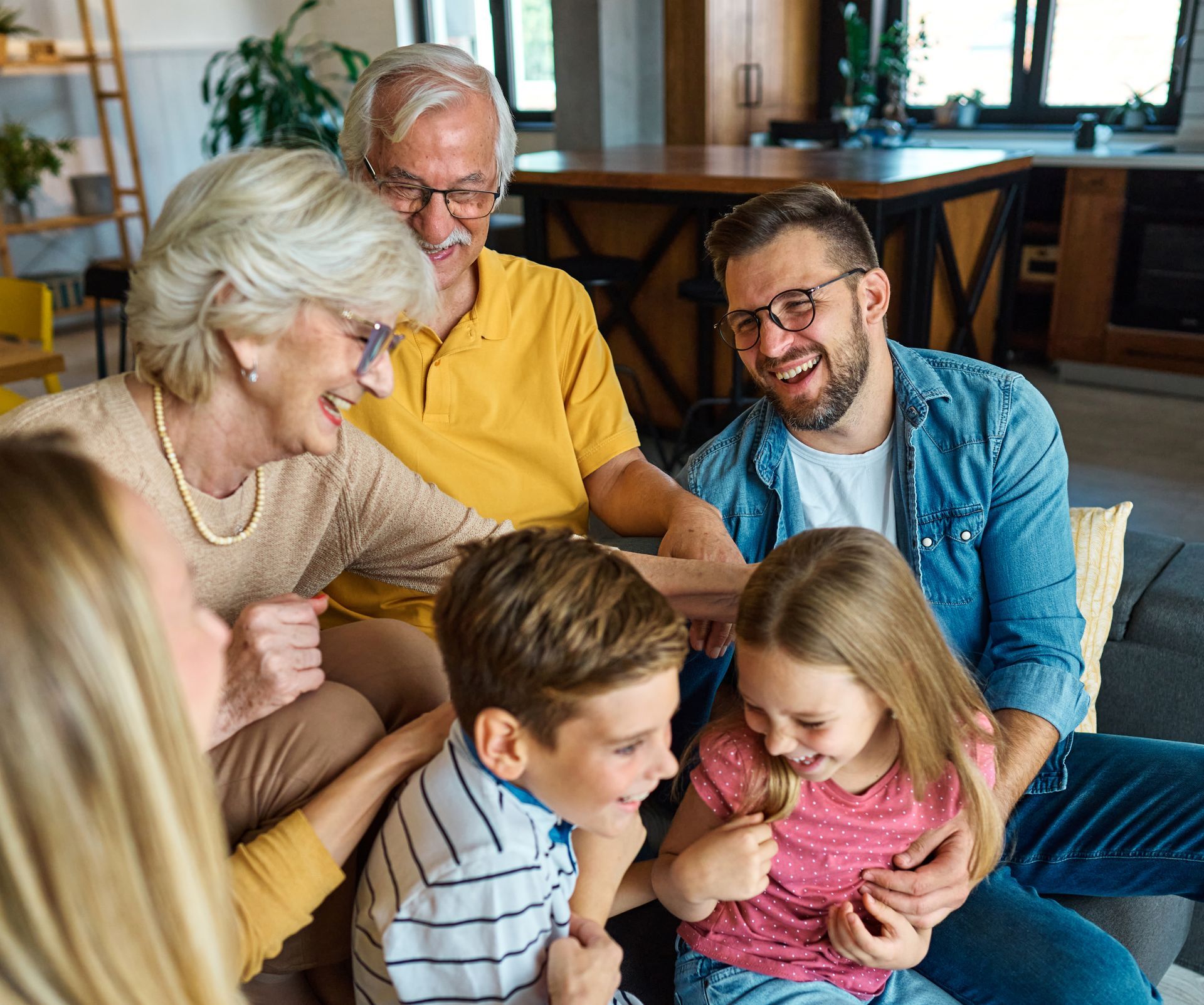 Family smiling together on a couch in a cozy living room, with grandparents and children gathered closely.