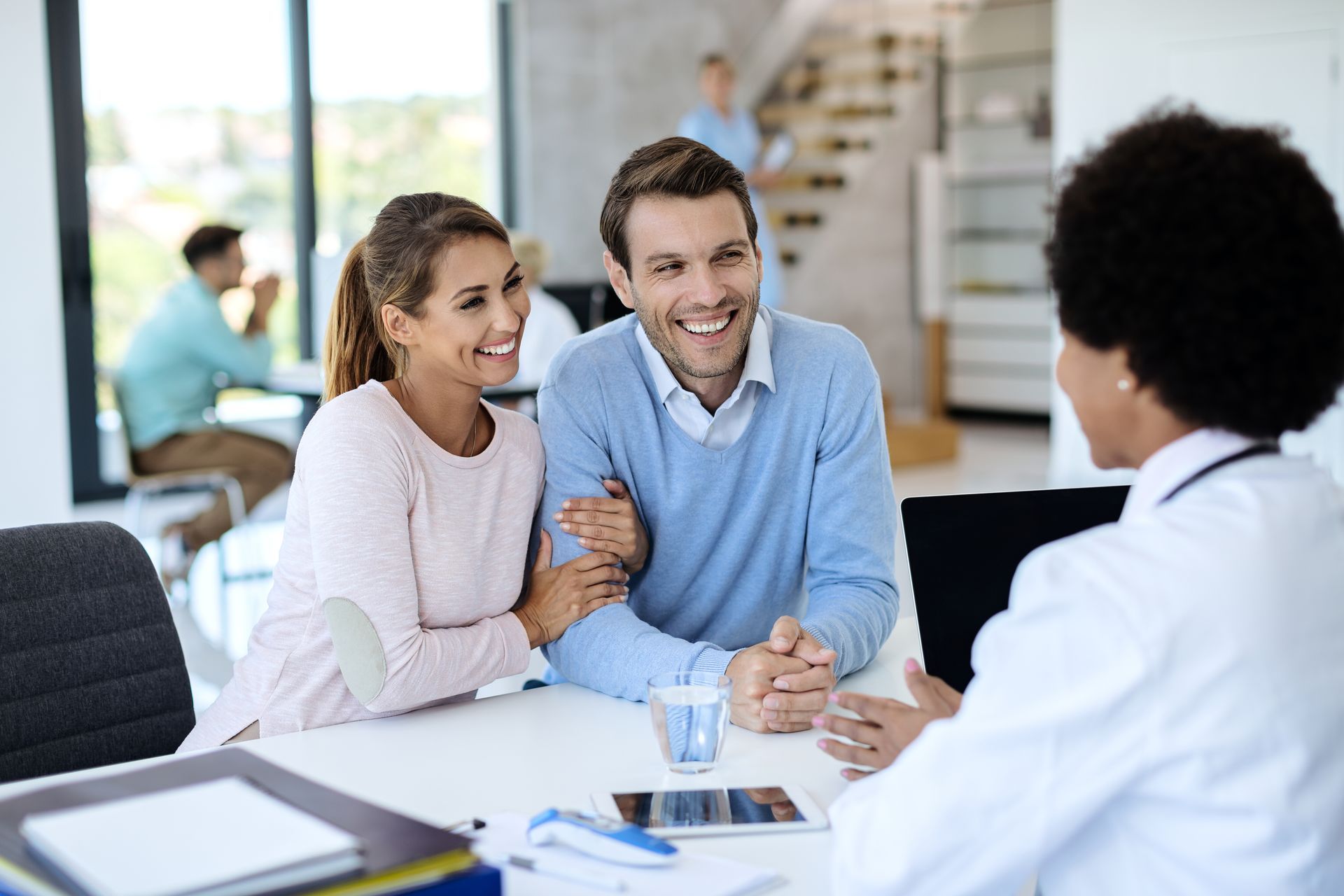 Two people smiling and talking across a desk with a counselor in a bright office