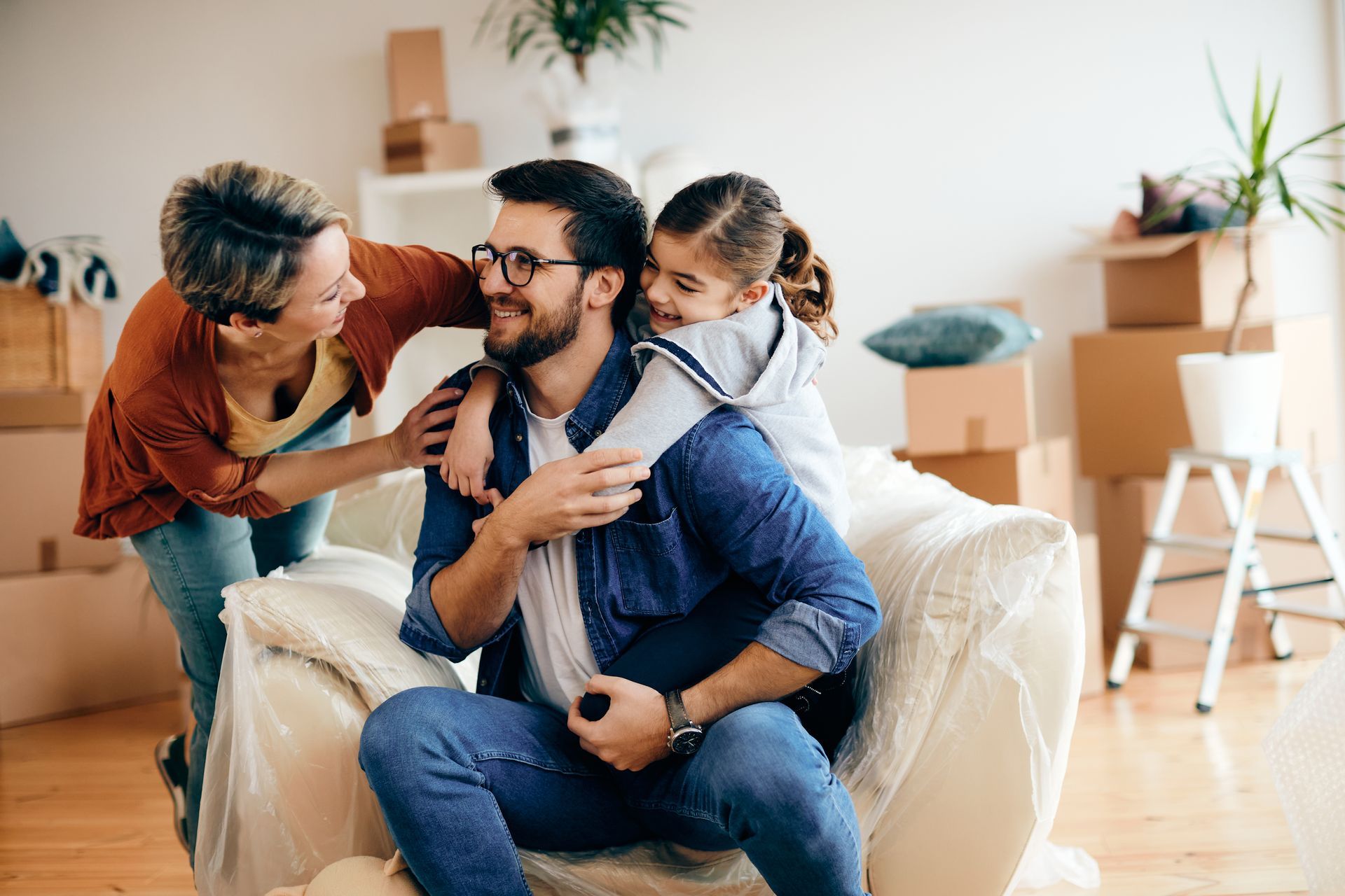 Two people smiling with a child on a couch in a bright living room, near moving boxes