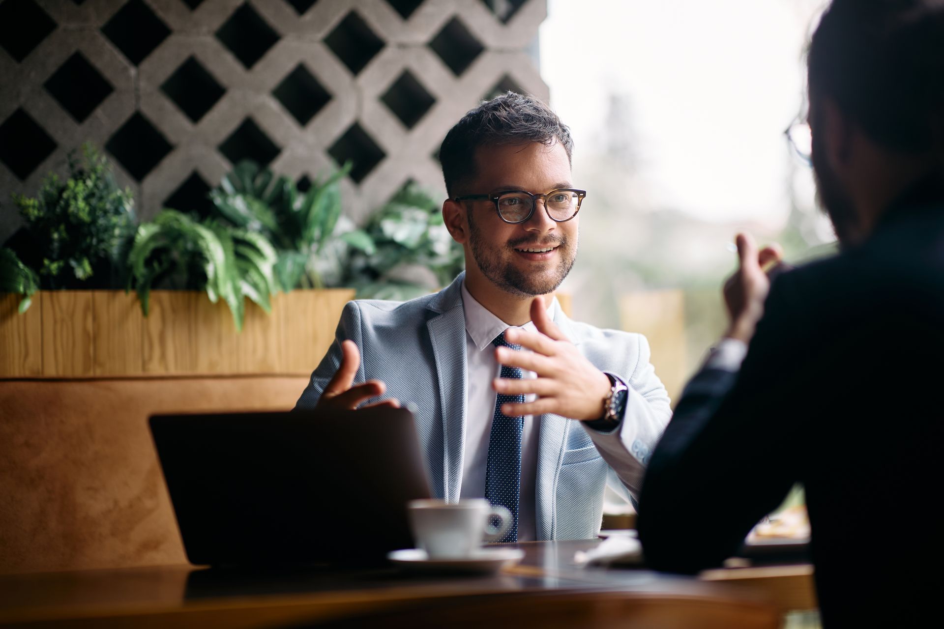 Two people talking at a café table with a laptop and coffee cup