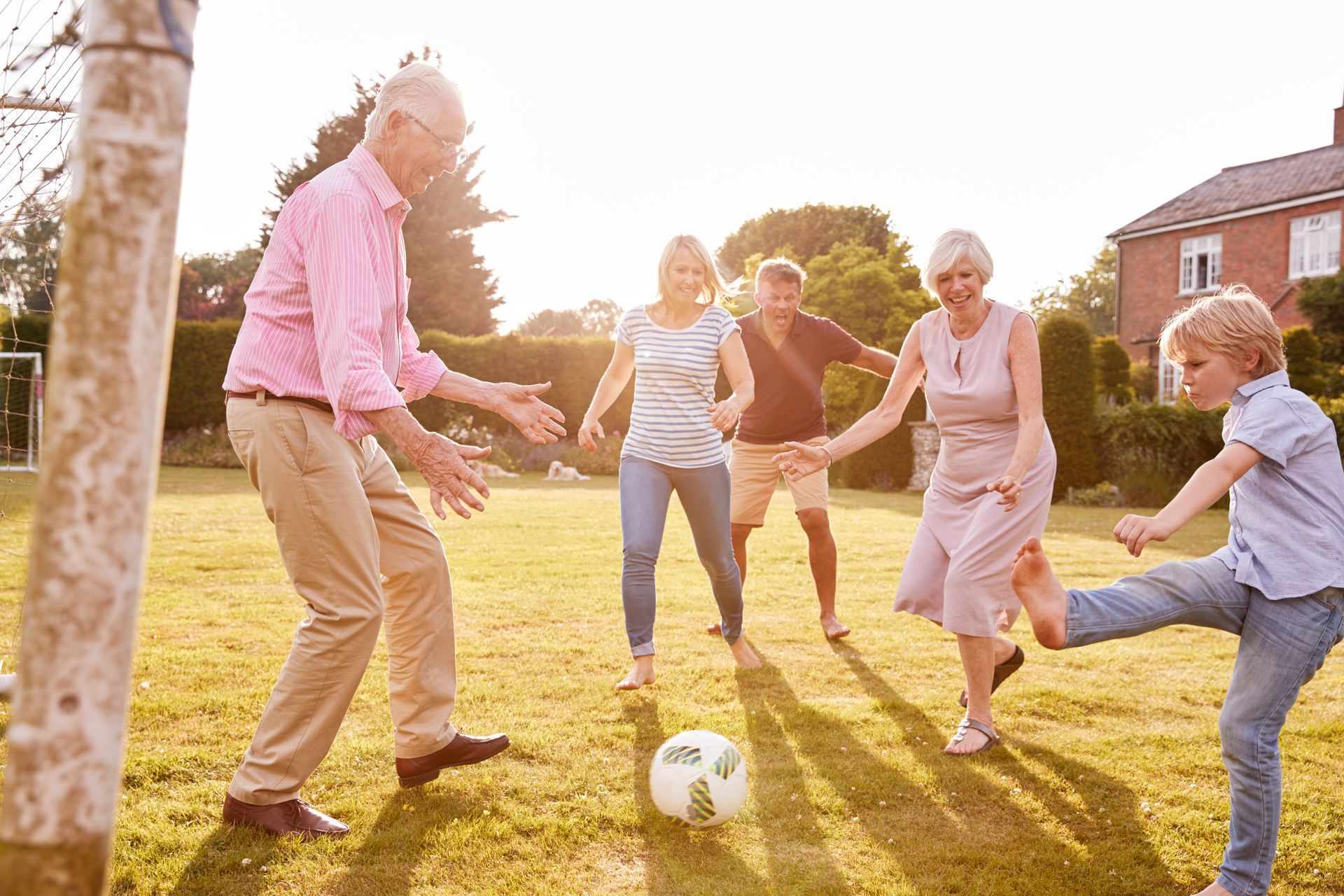 People playing soccer in a sunny backyard, with a ball in the center and houses in the background