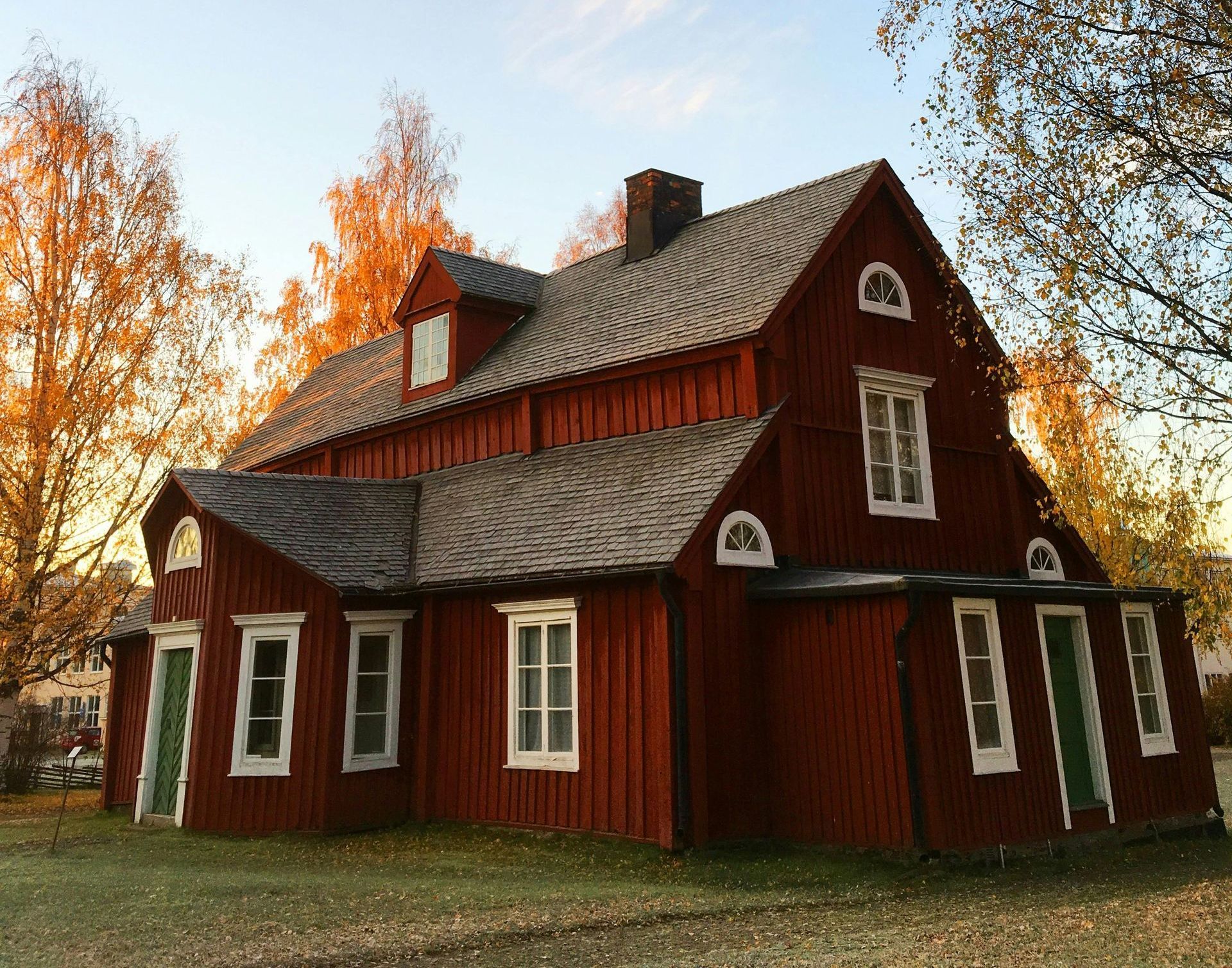 Red wooden farmhouse with white trim and a steep roof in an autumn yard