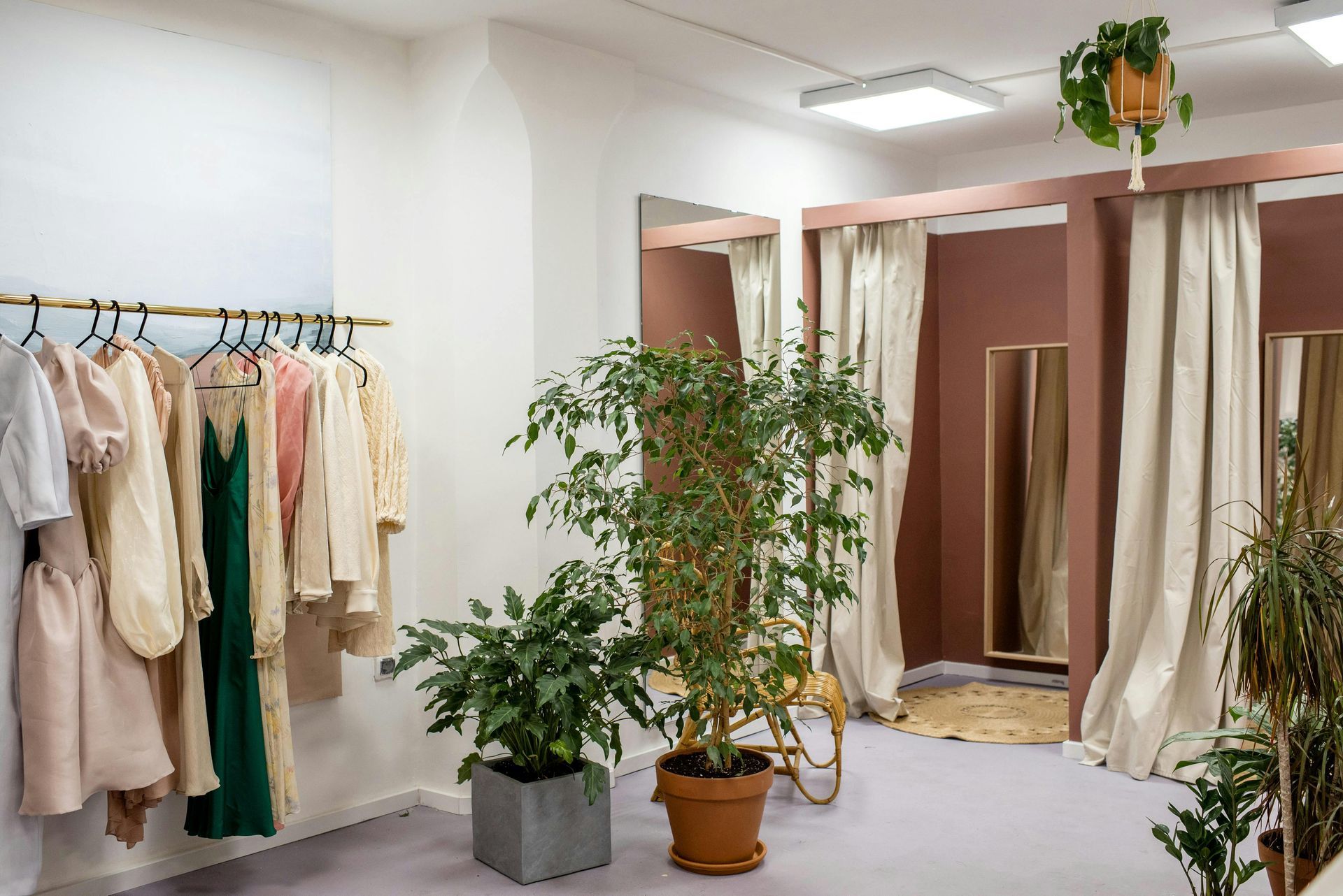 Minimalist clothing boutique with hanging garments, potted plants, and fitting rooms