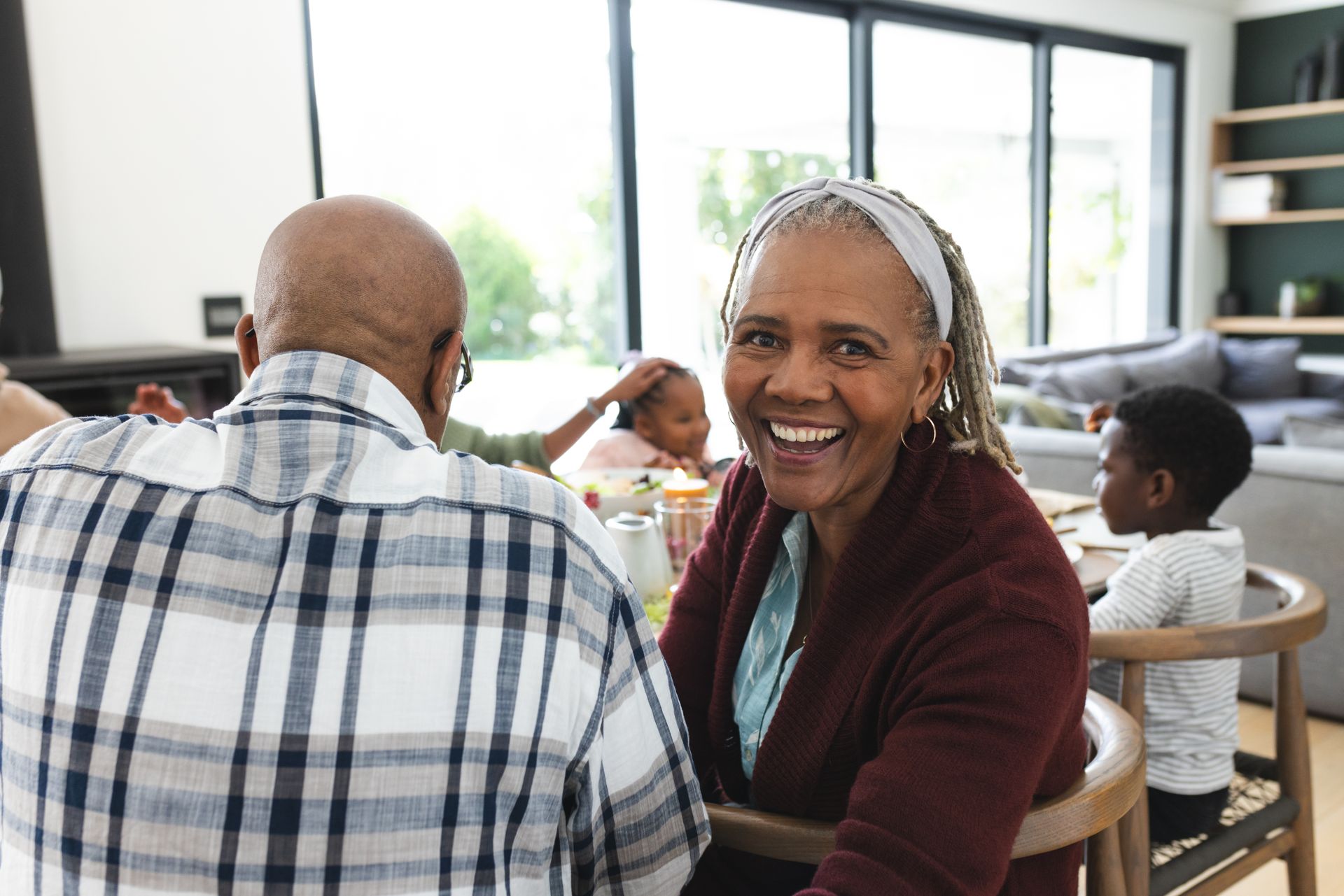 Smiling woman in a maroon sweater sits at a table in a bright room with other people nearby