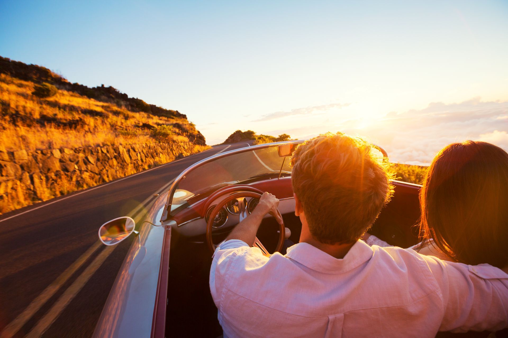 Couple riding in a convertible at sunset along a coastal road