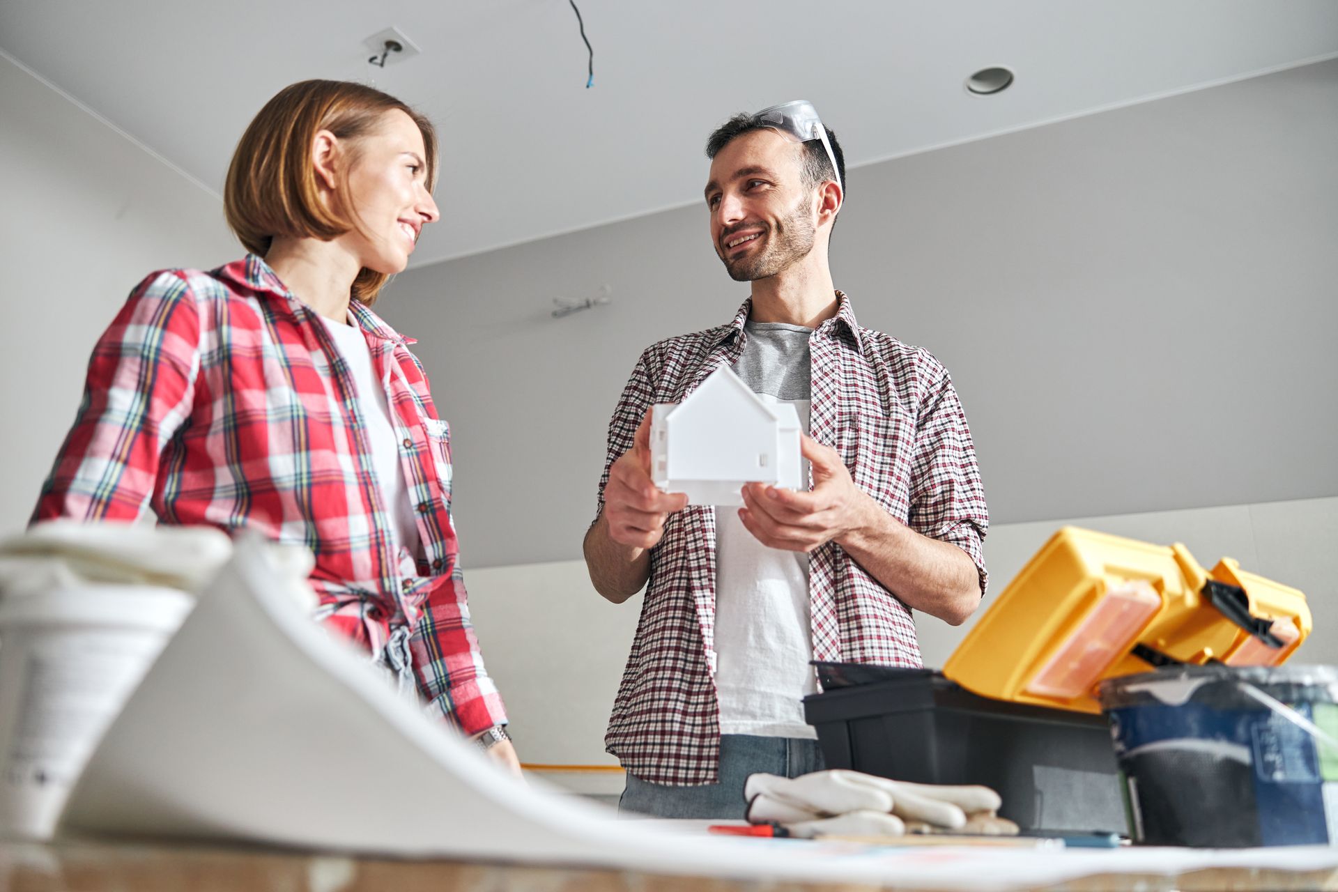 Two people discussing a home renovation plan in a room with tools and paint supplies