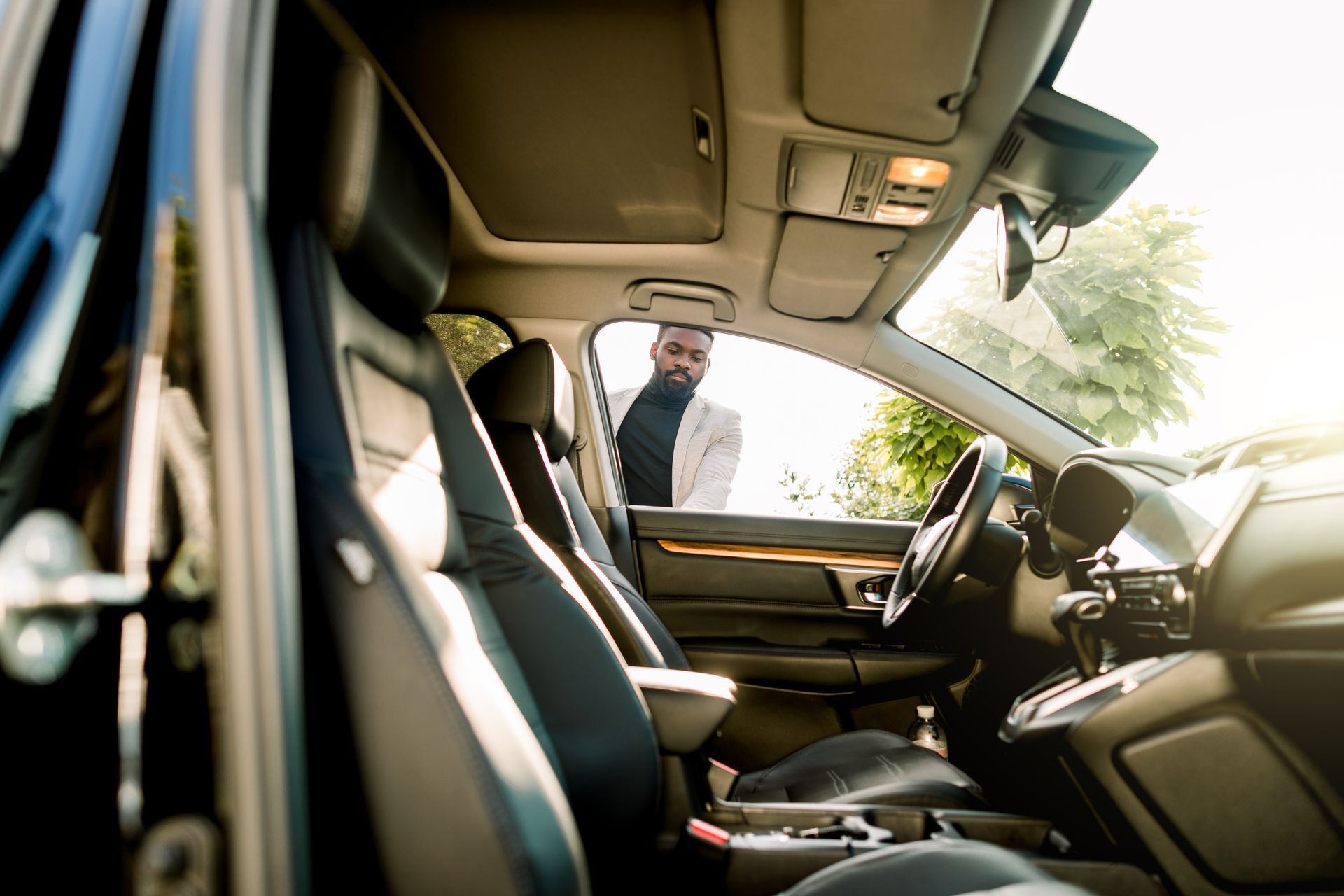 View from inside a car with the driver’s door open; a man stands outside by the window.