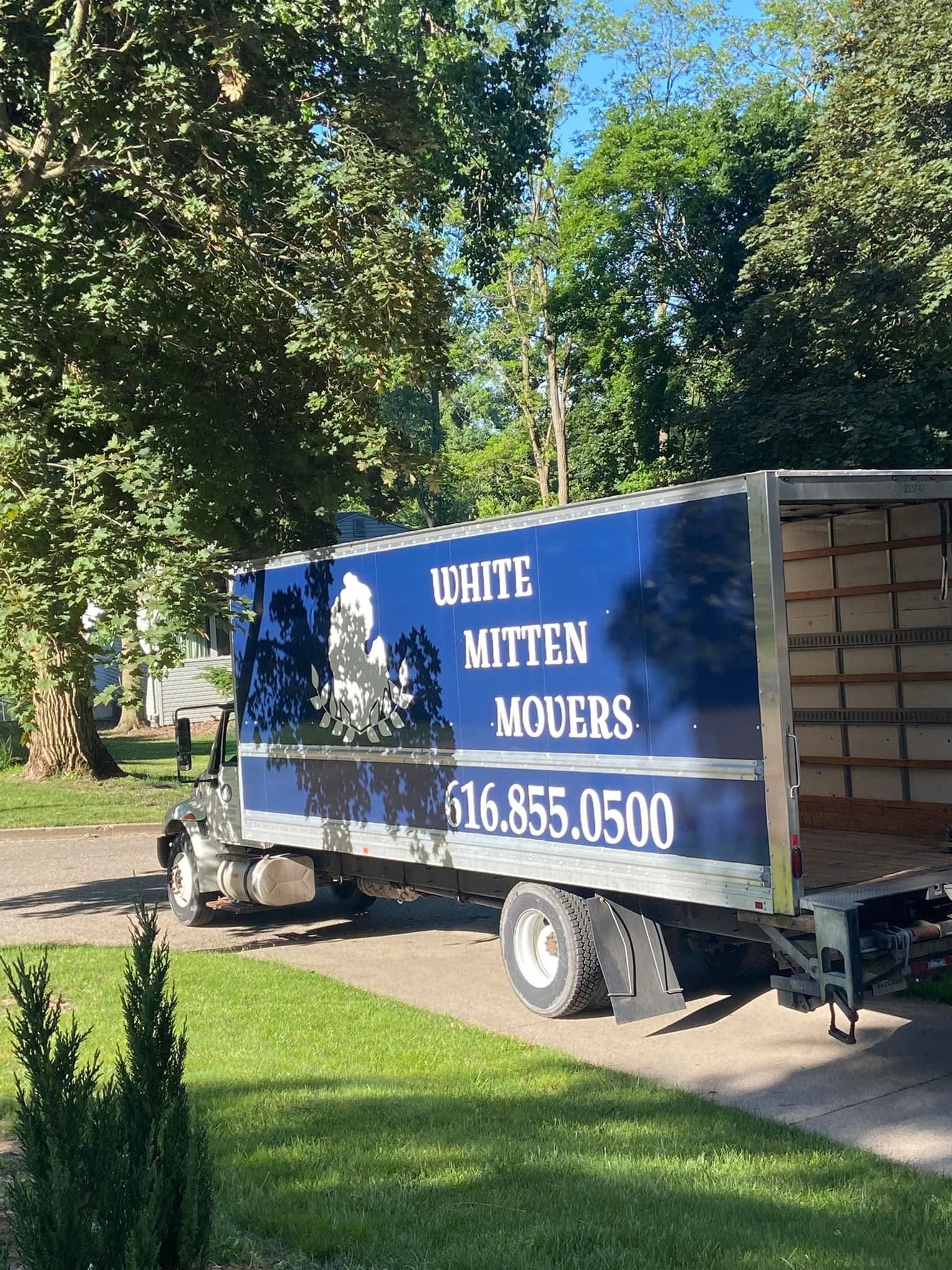 Blue moving truck parked on a driveway beside a grassy yard and trees