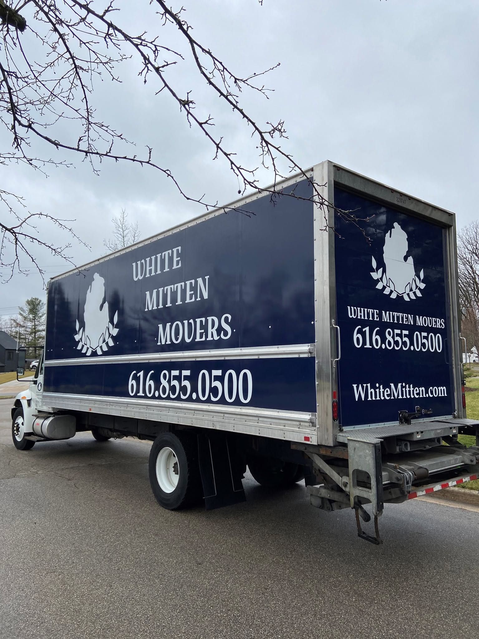 White movers truck parked outdoors with company logo and contact number on the side.