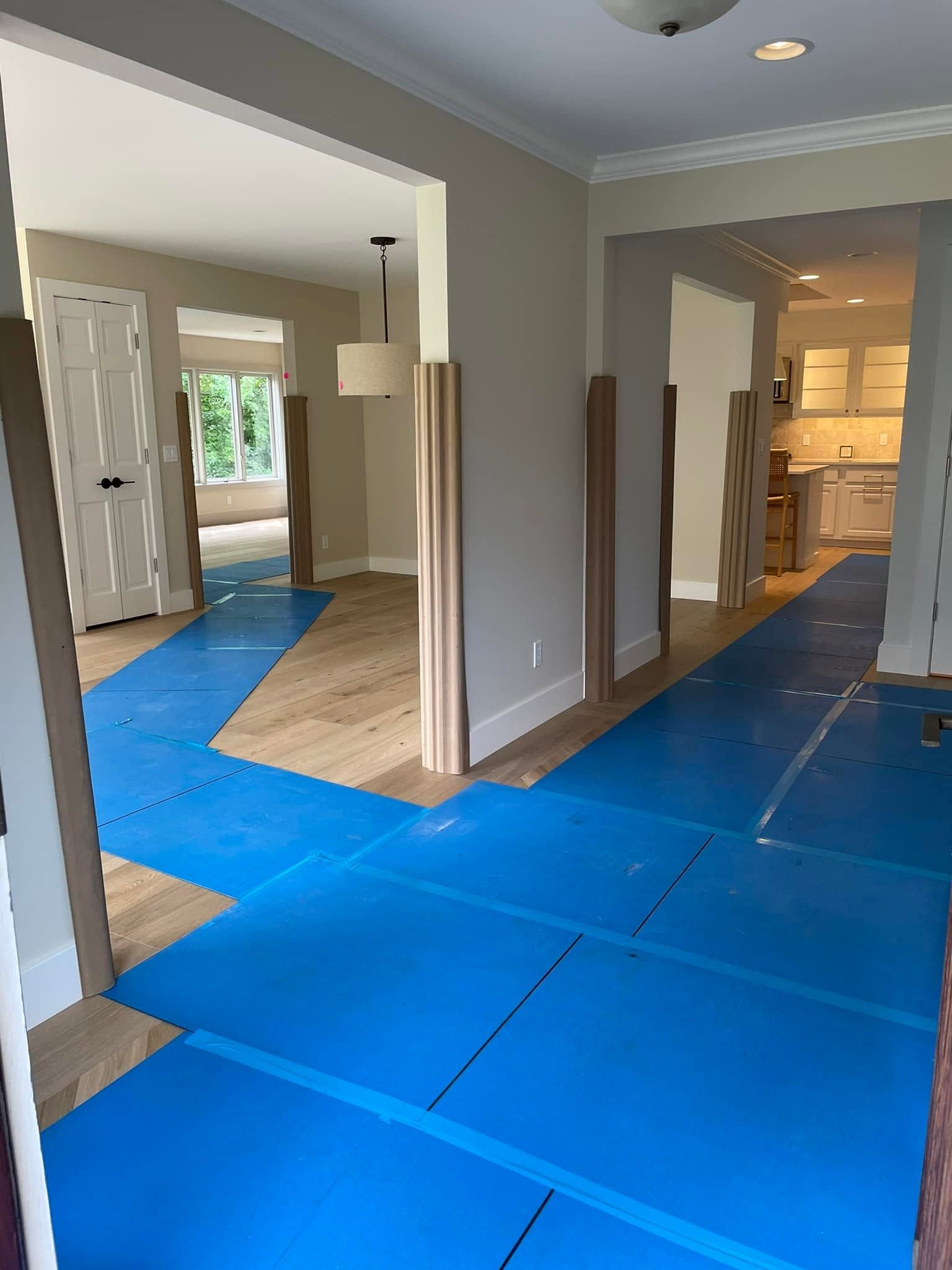 Room under renovation with blue floor protection, open doorways, and kitchen visible in the background