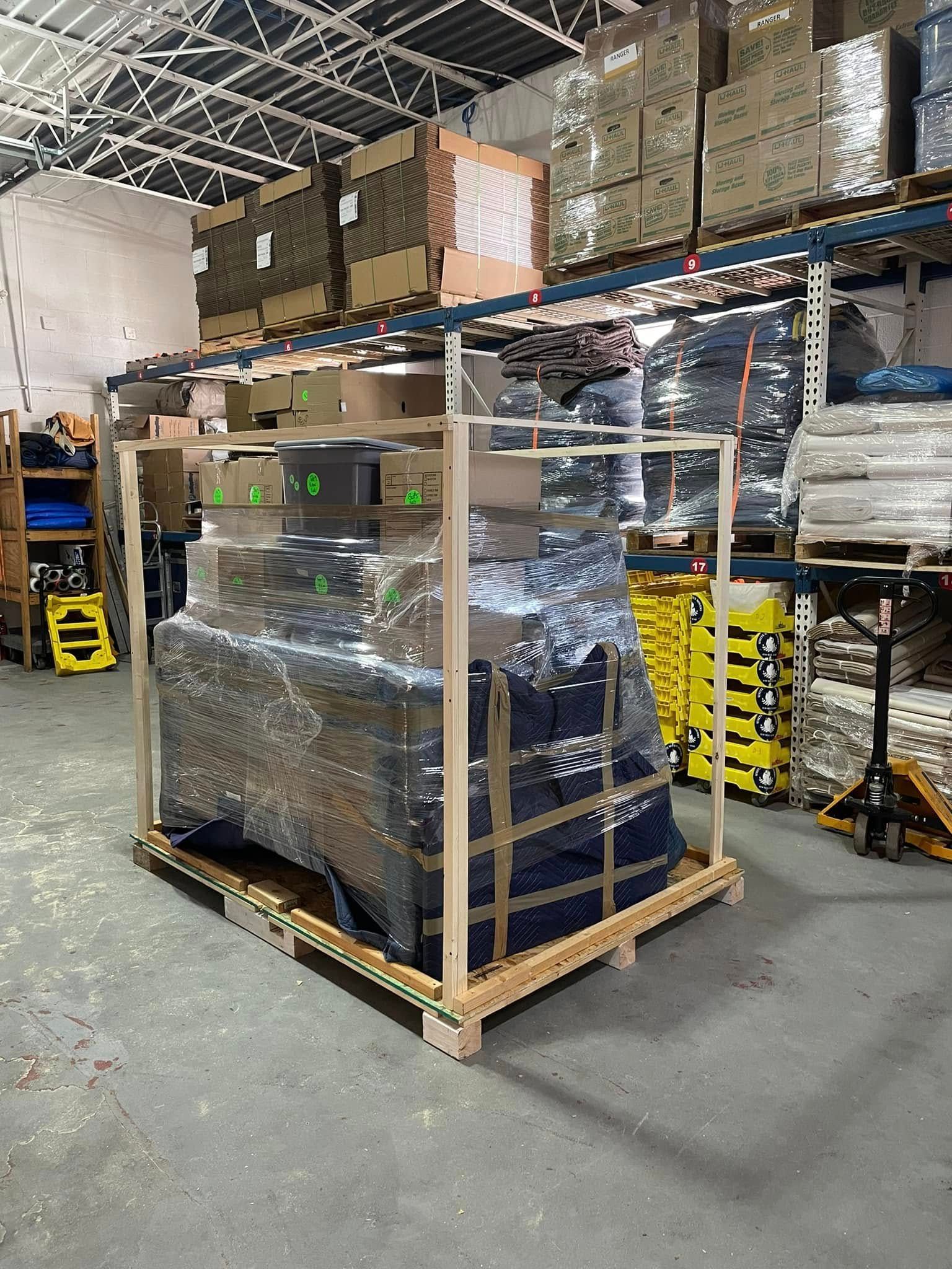 Warehouse pallet of shrink-wrapped goods on a wooden crate, with stacked boxes on a shelf above.