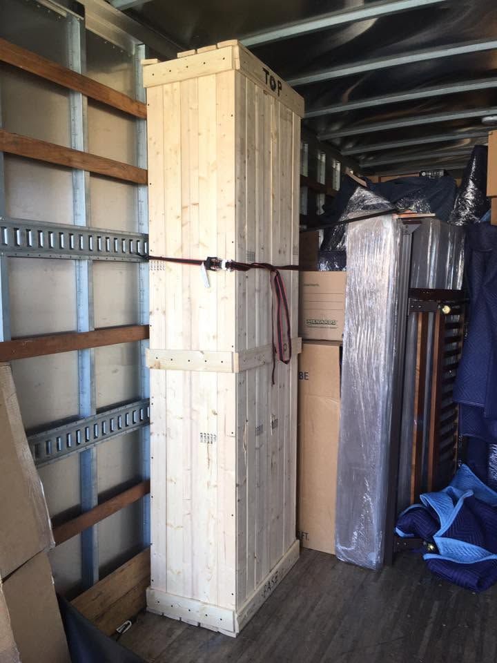 Interior of a cargo truck with stacked wooden crates, wrapped items, and shelving along the left wall