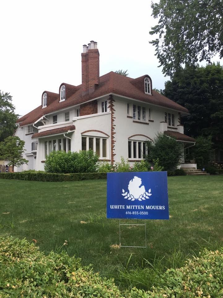 White house with red roof and chimney behind a blue sign in a grassy yard
