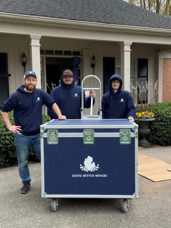Three workers stand behind a blue equipment case on a cart outside a house.