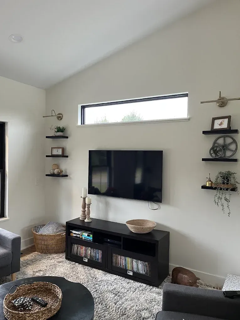 Modern living room with wall-mounted TV, floating shelves, black media console, and woven baskets on a light rug