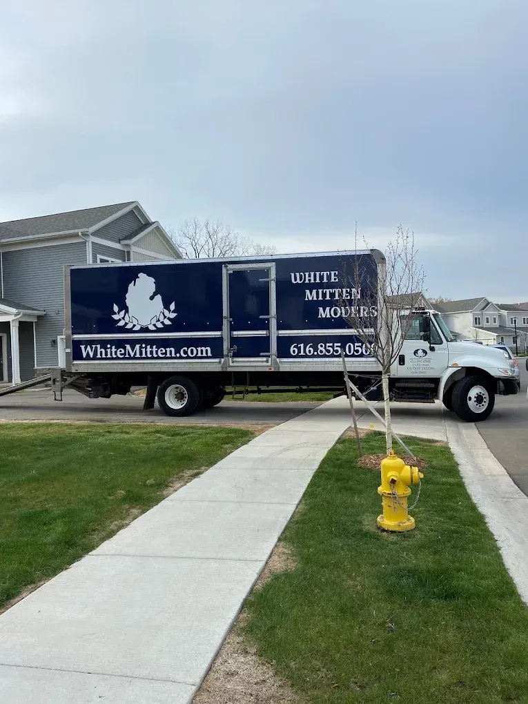 White Mighty Movers truck parked by a suburban sidewalk near a yellow fire hydrant