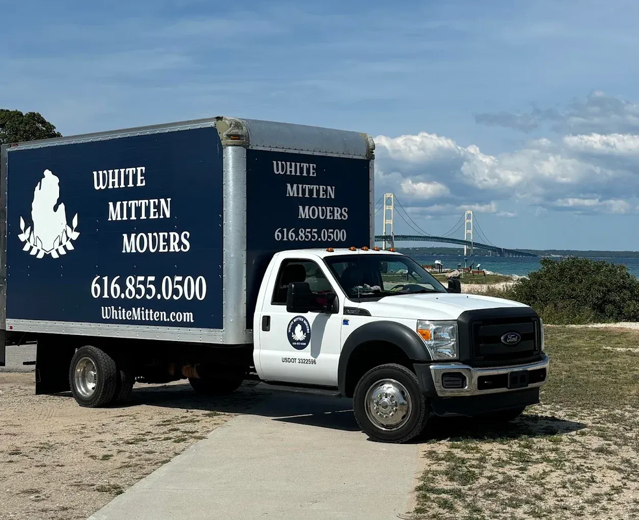 White trash removal truck parked by the water with blue company signage and phone number visible