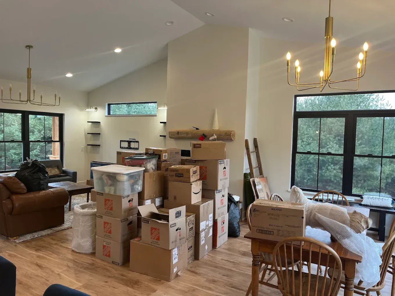Living room packed with moving boxes and furniture under bright windows and chandeliers