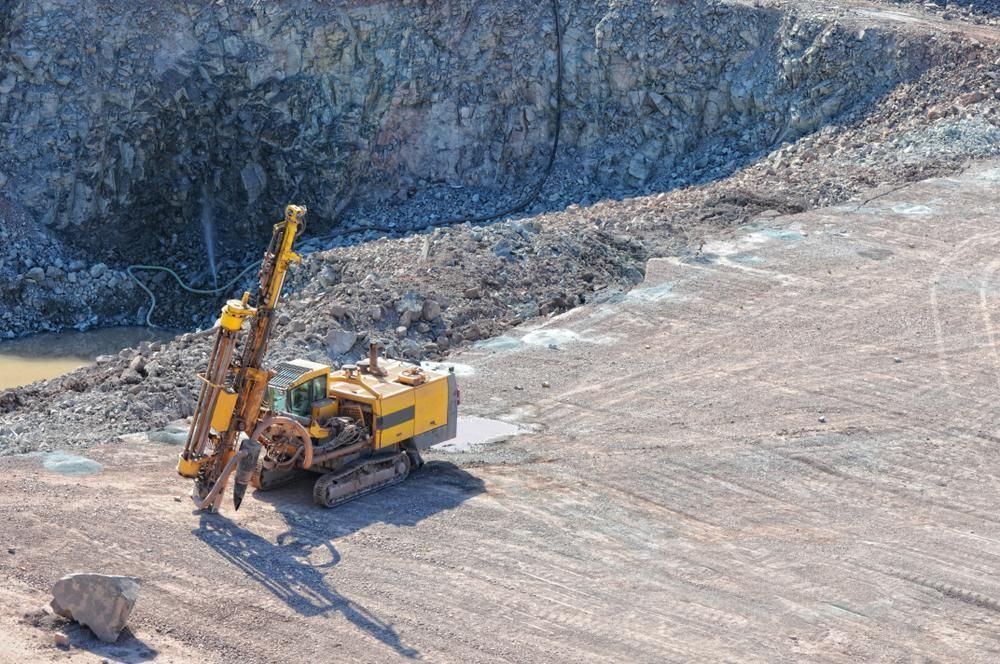 A Yellow Excavator Is Sitting in The Middle of A Dirt Field in A Quarry — Hillery Group in Bowen, QLD