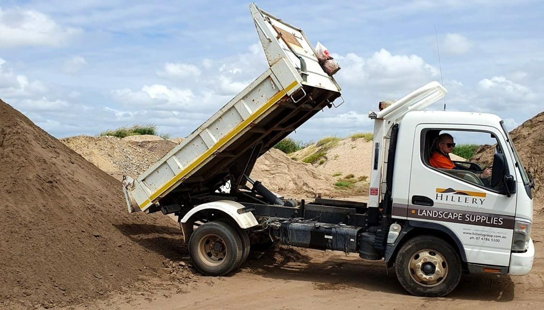 A Man Is Driving a Dump Truck in A Dirt Field — Hillery Group in Belmore, NSW