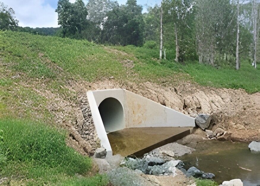 A Concrete Pipe Is Going Through a Stream Next to A Grassy Hill — Hillery Group in Bowen, QLD