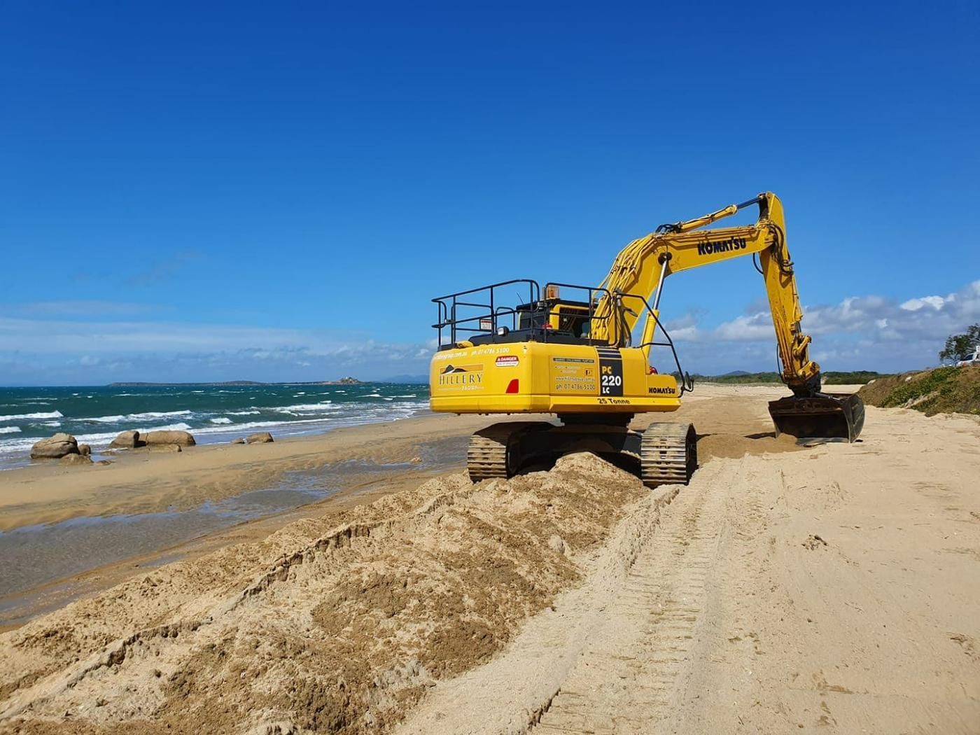 A Yellow Excavator Is Working on A Sandy Beach Near the Ocean  — Hillery Group in Bowen, QLD