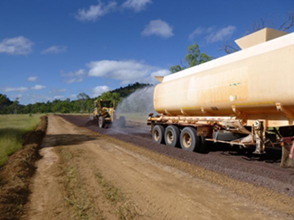 A Tanker Truck Is Spraying Water on A Dirt Road — Hillery Group in Belmore, NSW
