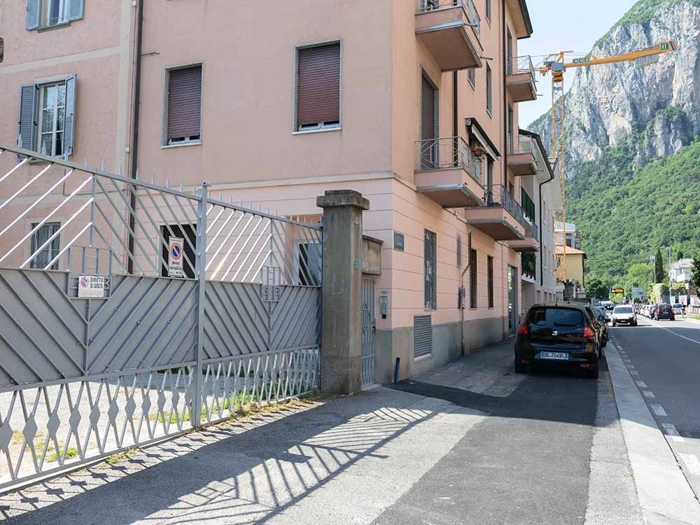 Stretta via accanto a un palazzo color pesca, con un'auto nera parcheggiata e scogliere montuose sullo sfondo.