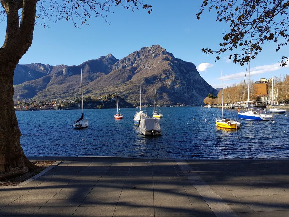 Colorato villaggio lacustre con barche sull'acqua cristallina e montagne sotto un cielo azzurro.