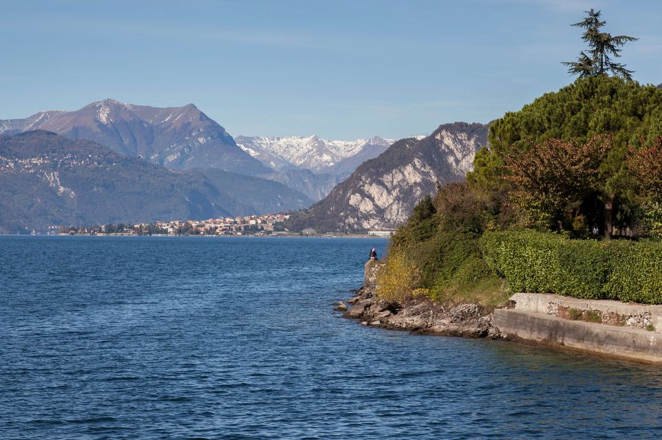 Lago di montagna dalle acque azzurre, cime innevate in lontananza e una costa rocciosa e verdeggiante sotto un cielo limpido.