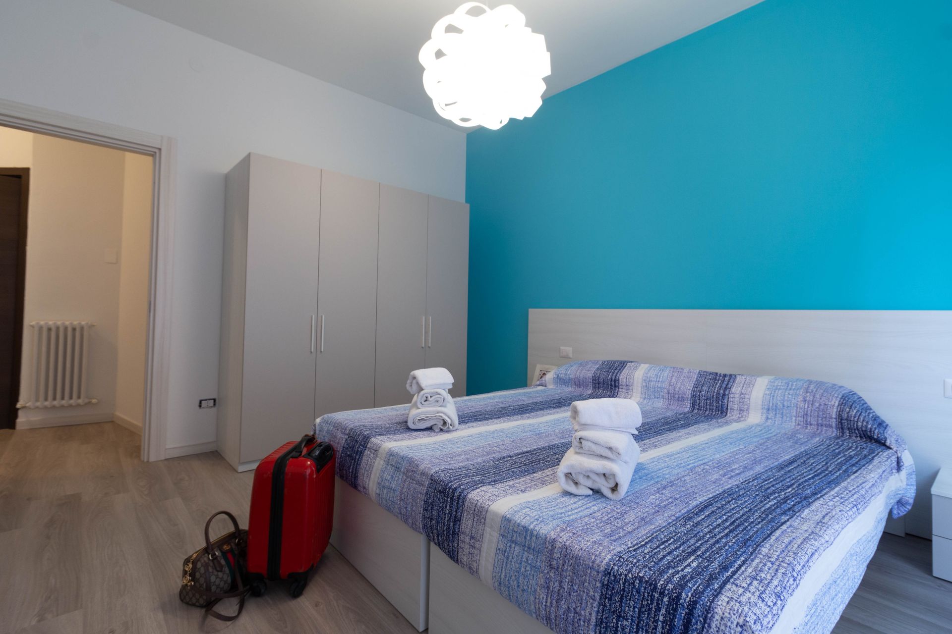 Piccola camera da letto con letto, parete con dettagli blu, armadio e valigie vicino alla porta.