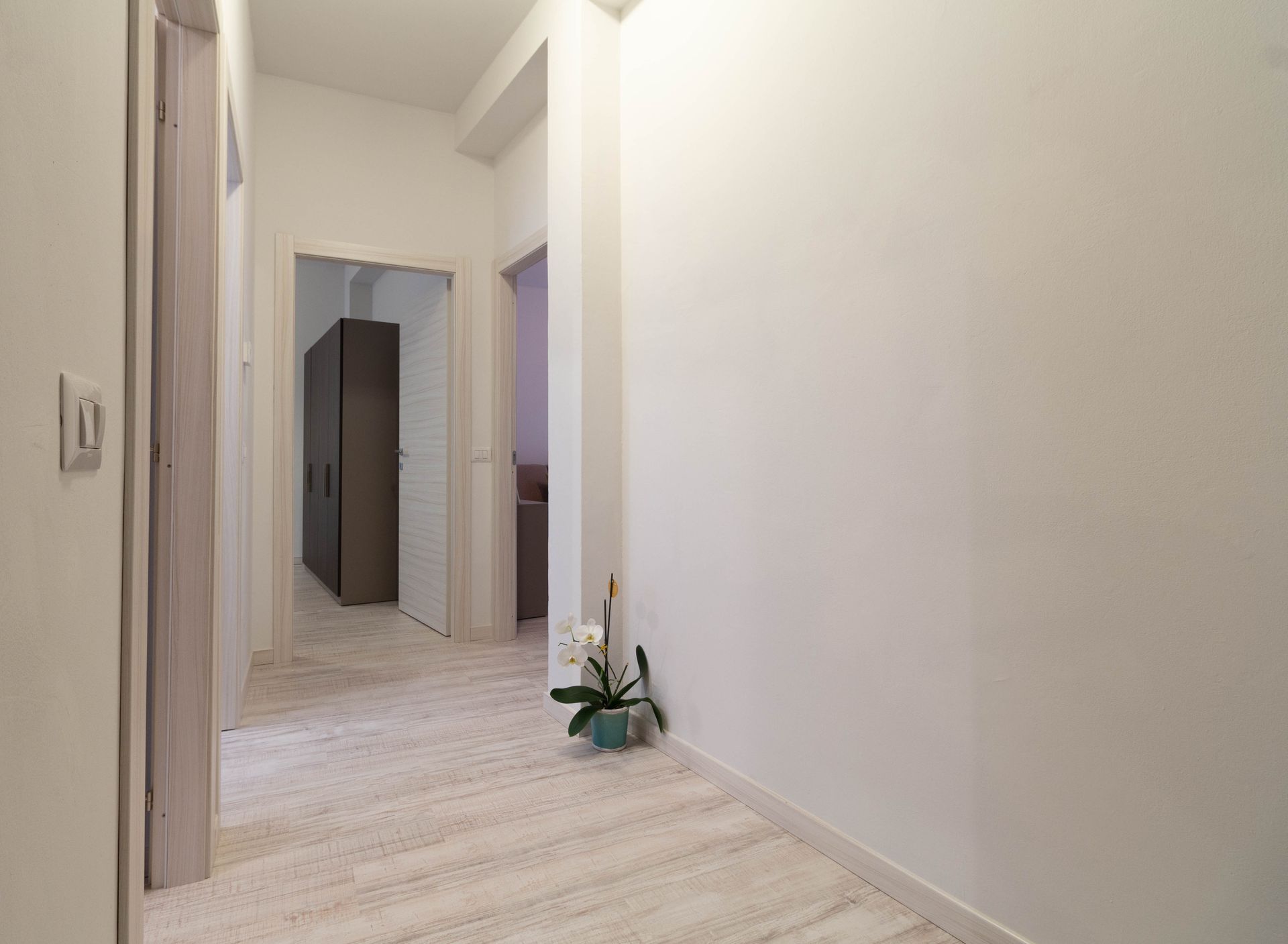 Luminosa sala da pranzo-soggiorno moderna con tavolo rotondo, divano grigio, TV a parete e tende trasparenti vicino alla porta del balcone.
