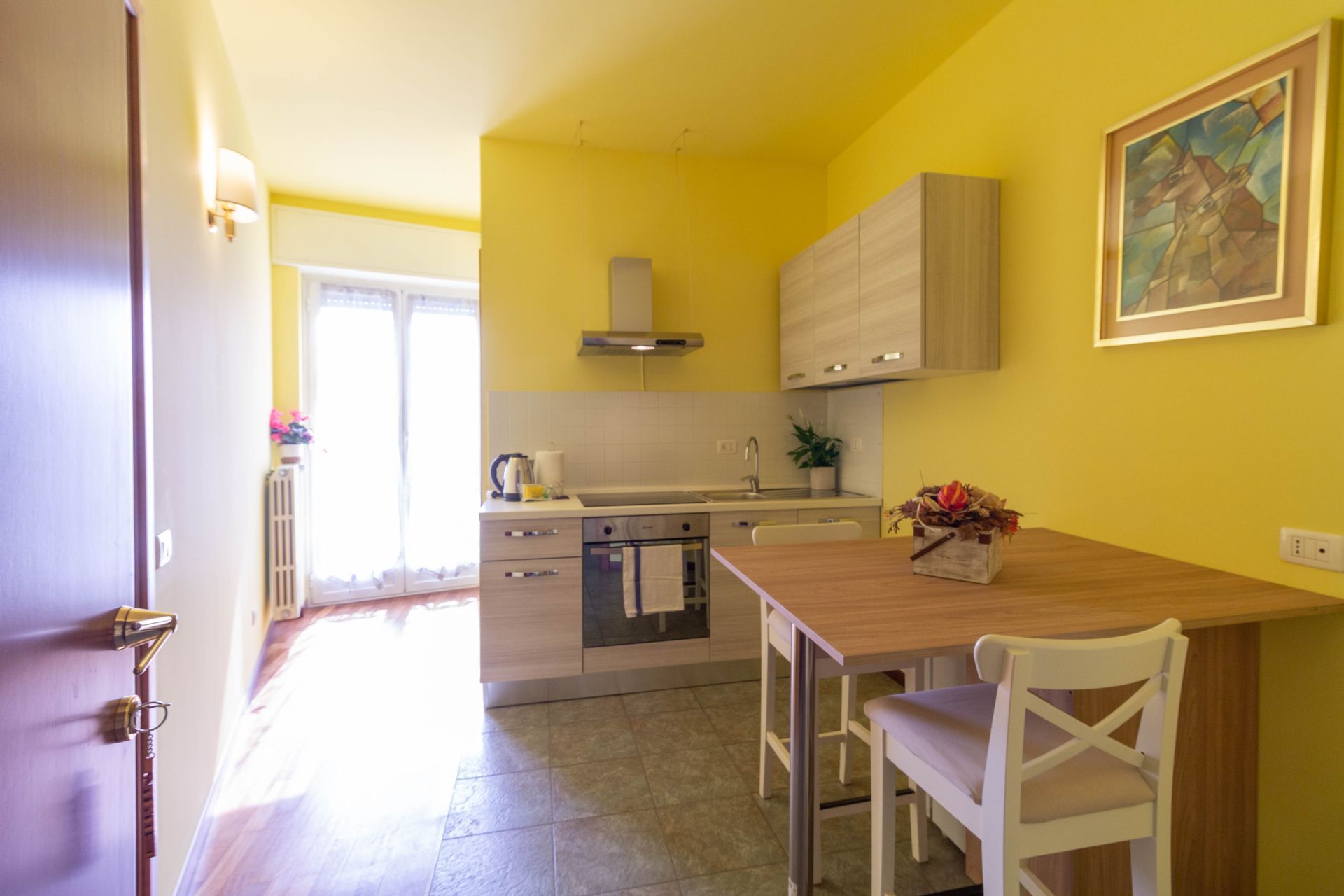 Camera d'albergo pulita e ordinata, con letto matrimoniale, lampada da comodino, finestra e mobili in legno.