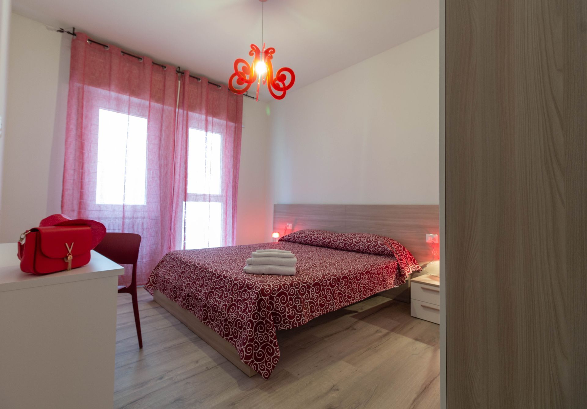 Camera d'albergo pulita e ordinata, con letto matrimoniale, lampada da comodino, finestra e mobili in legno.