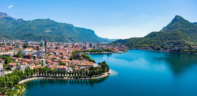 Cittadina lacustre con edifici colorati e montagne verdi sotto un cielo azzurro limpido.