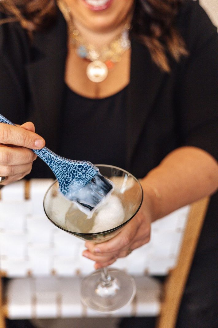 Woman stirring a white frothy drink in a stemmed glass with a blue patterned utensil.